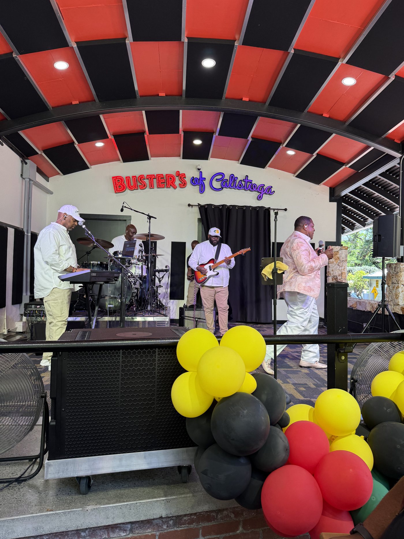 Live band on the Busters of Calistoga stage with red, yellow, green, and black balloon arch, 2025 Freedom Ride